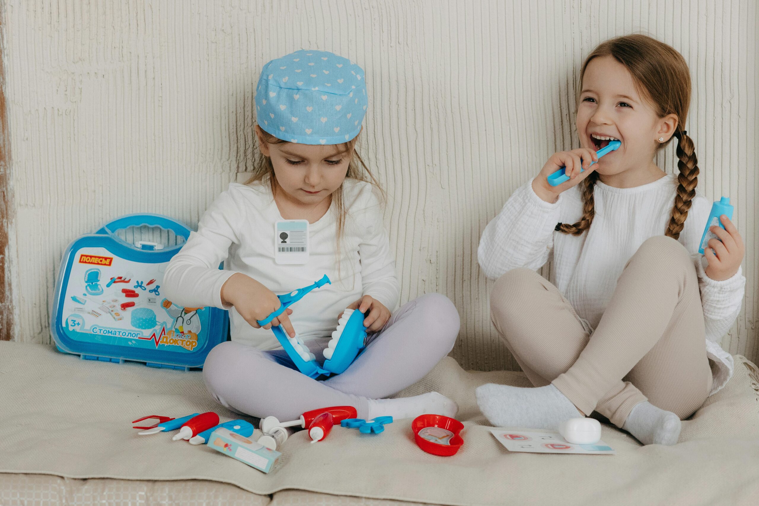 Two young girls having fun playing dentist with a toy kit indoors, enjoying imaginative play.